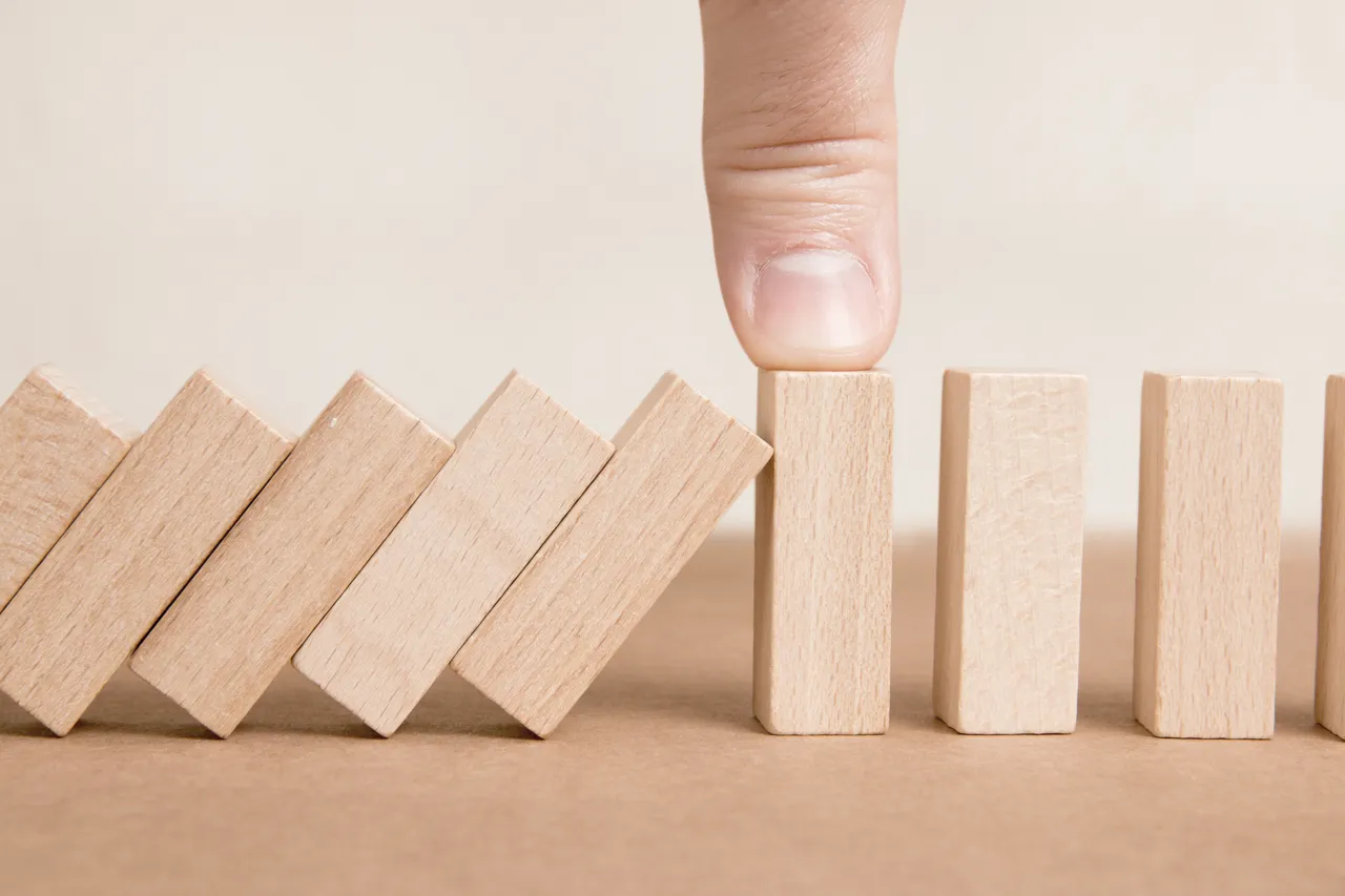 Wooden Blocks one of them held by a human finger preventing another ones from falling. Concept of Risk Management, Reliability, Protection and Business Stability.