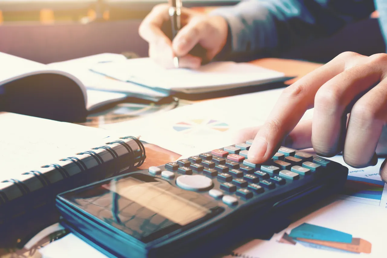 Close up woman hand pressing calculator and doing finance at home office with writing make note report on notebook.